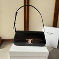 Black handbag with gold clasp on a white box, with a Celine bag in the background.