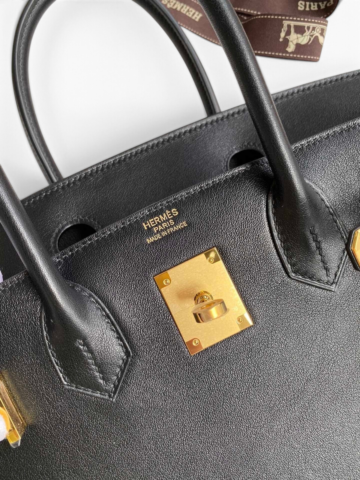 SWORD LUXURY imzalı, altın donanımlı ve ikonik kilit detayına sahip siyah Swift dana derisi Hermès Birkin 25cm çanta.