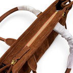 SWORD LUXURY kahverengi süet çanta, altın rengi fermuar detaylı ve koruyucu ambalajlı saplara sahip üstten görünüm.