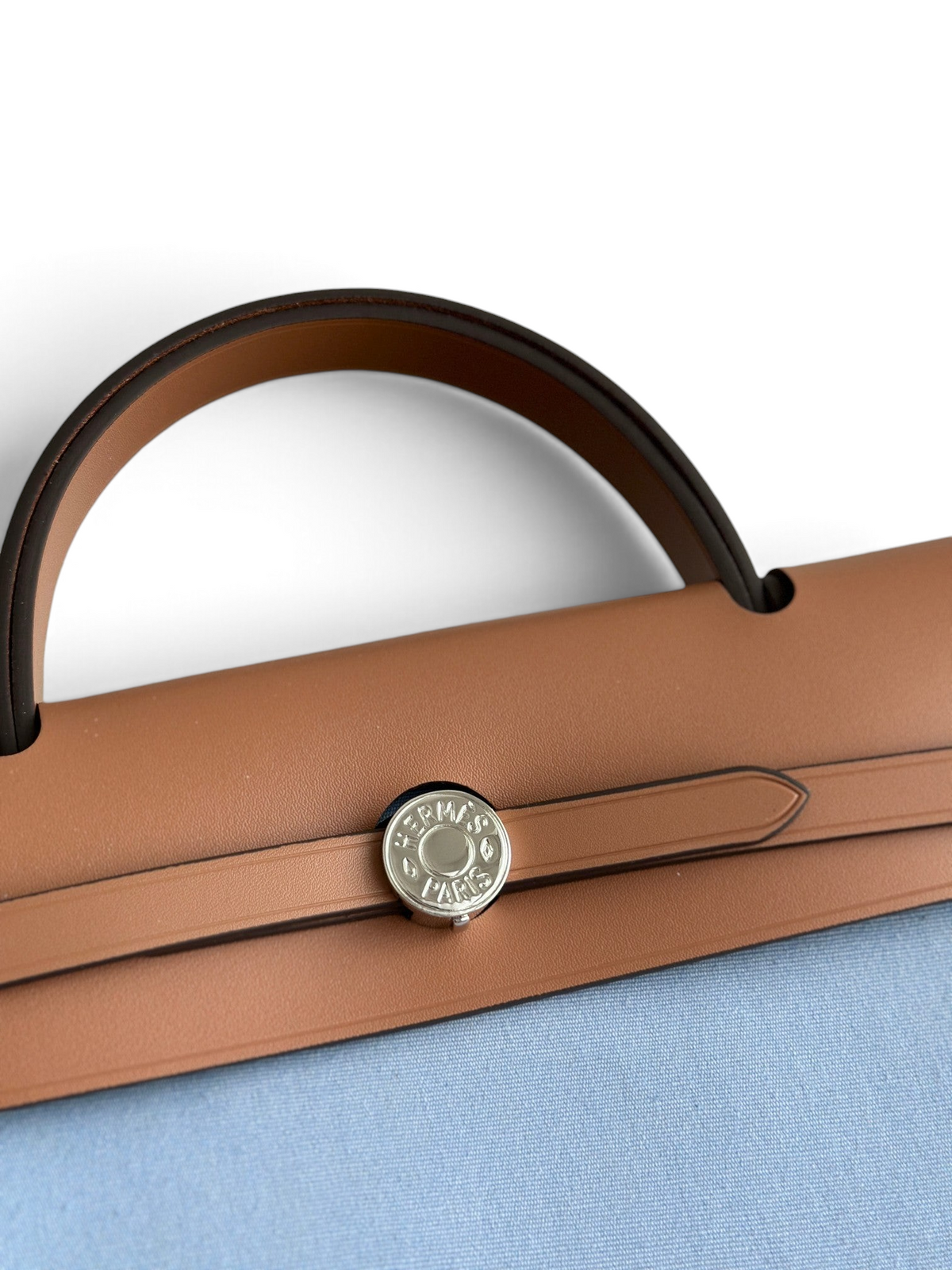 SWORD LUXURY Hermès Herbag 31 çanta, kahverengi deri kapaklı, gümüş Clou de Selle kilit detaylı ve mavi kanvas gövdeli.