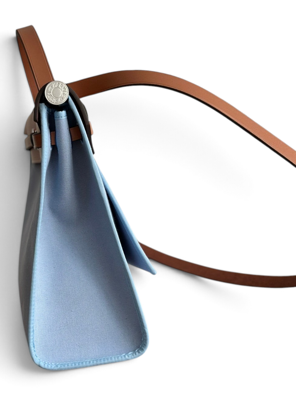 SWORD LUXURY marka, açık mavi kanvas ve taba rengi deri detaylı, yan profilden görünen şık Hermès Herbag 31 çanta.