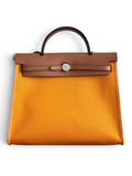 SWORD LUXURY Hermès Herbag 31 çanta, turuncu kanvas gövde ve kahverengi deri kapak detaylı, şık ve modern tasarım.