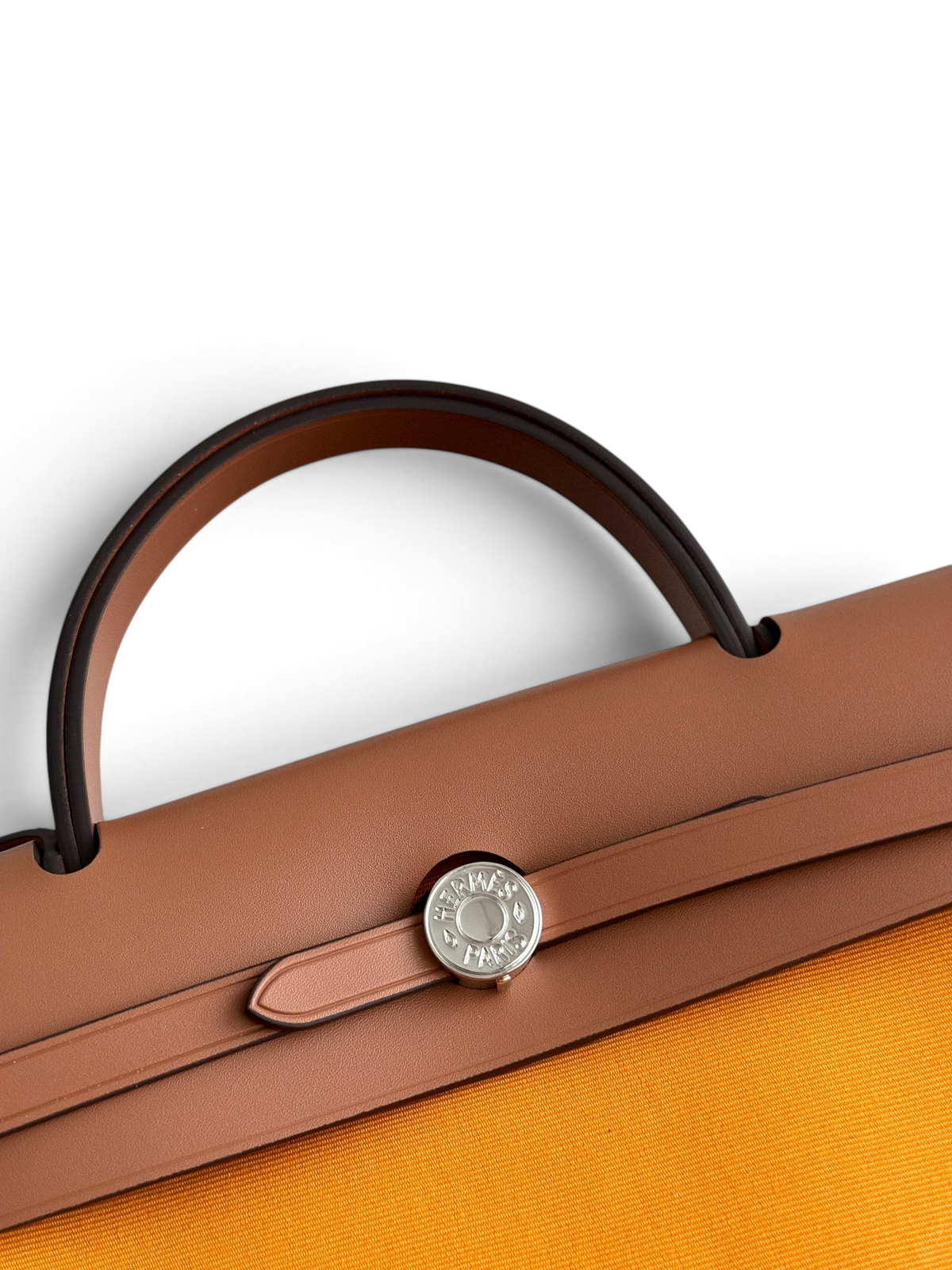 SWORD LUXURY Hermès Herbag 31 çanta, taba rengi deri kapaklı, gümüş Clou de Selle kilit detaylı ve turuncu kanvas gövdeli.
