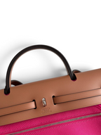 SWORD LUXURY Hermès Herbag 31 çanta, kahverengi deri kapaklı ve canlı pembe kanvas gövdeli, Clou de Selle detaylı.
