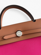 SWORD LUXURY Hermès Herbag 31 çanta, taba rengi deri kapaklı ve canlı pembe kanvas gövdeli, gümüş Clou de Selle detaylı.