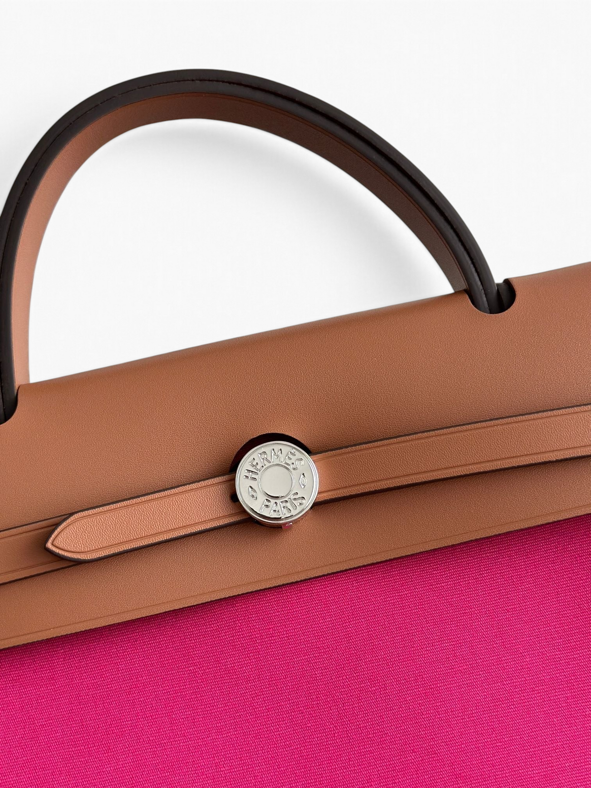 SWORD LUXURY Hermès Herbag 31 çanta, taba rengi deri kapaklı ve canlı pembe kanvas gövdeli, gümüş Clou de Selle detaylı.