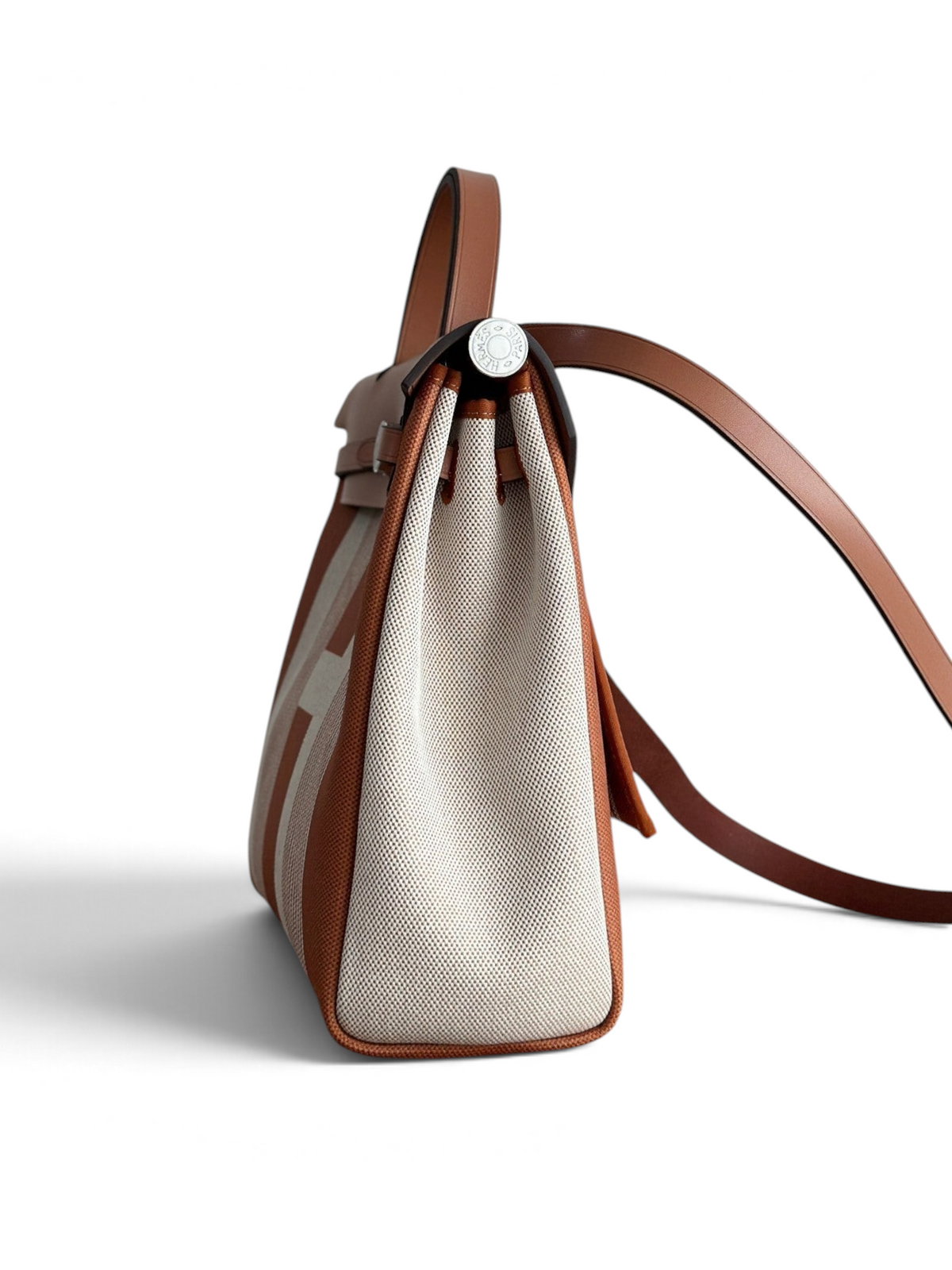 SWORD LUXURY Hermès Herbag 31 çanta, taba rengi deri detaylı ve bej kanvas gövdeli, yan profilden görünüm.
