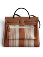 SWORD LUXURY Hermès Herbag 31 çanta, kahverengi ve beyaz çizgili kanvas gövde, deri kapak ve Clou de Selle detaylı.