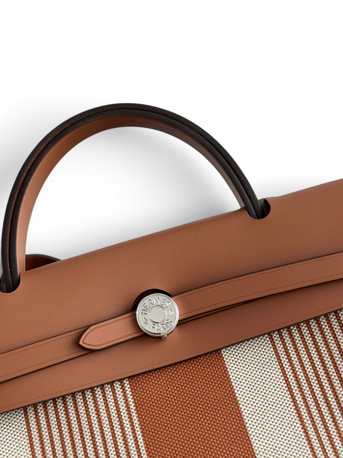 SWORD LUXURY Hermès Herbag 31 çanta, taba rengi deri kapaklı, Clou de Selle kilitli ve çizgili kanvas gövdeli detay.