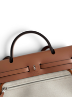 SWORD LUXURY Hermès Herbag 31 çanta, taba rengi deri kapaklı ve bej kanvas gövdeli, şık Clou de Selle detaylı.