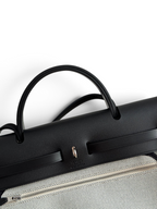 SWORD LUXURY Hermès Herbag 31 çanta, siyah deri kapaklı ve Clou de Selle kilit detaylı, şık kanvas gövde tasarımı.