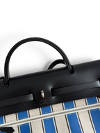 SWORD LUXURY Hermès Herbag 31 çanta, siyah deri kapaklı ve mavi çizgili kanvas gövdeli, Clou de Selle detaylı.