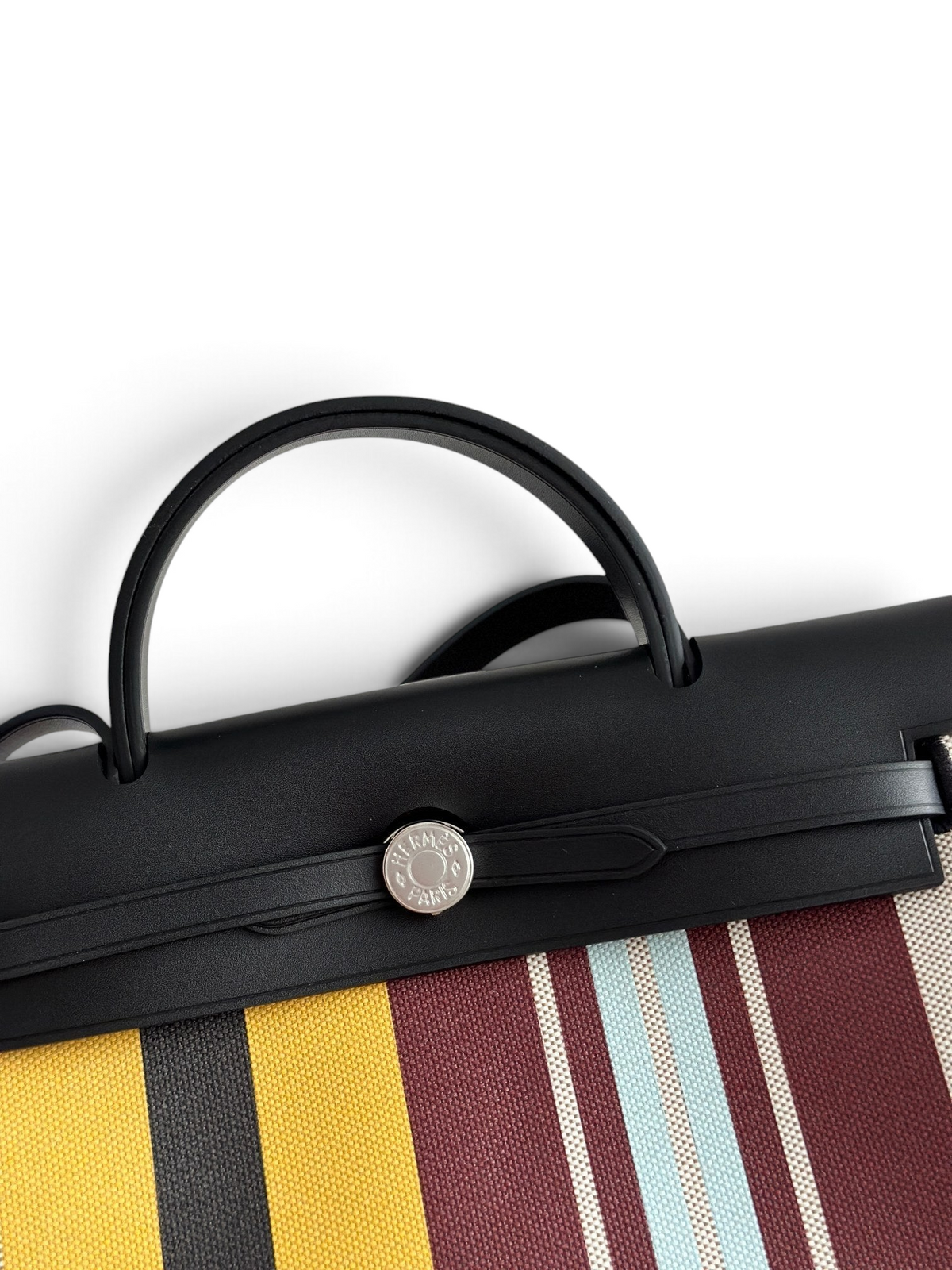 SWORD LUXURY Hermès Herbag 31 çanta, siyah deri kapaklı, renkli çizgili kanvas gövdeli ve gümüş Clou de Selle detaylı.