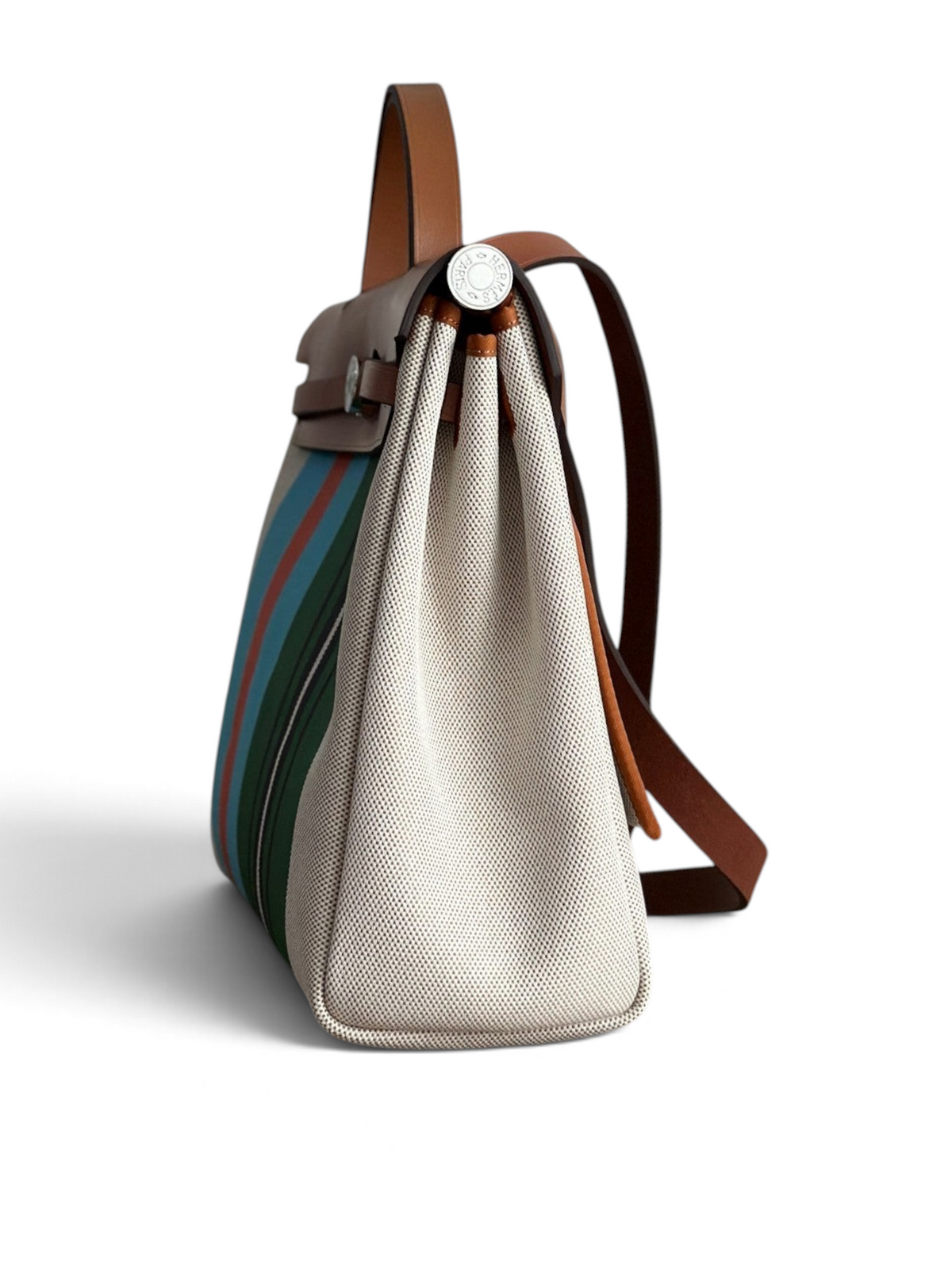 SWORD LUXURY Herbag 31 çanta, yan profilden görünüm, bej kanvas gövde, renkli çizgili detaylar ve kahverengi deri kapak.