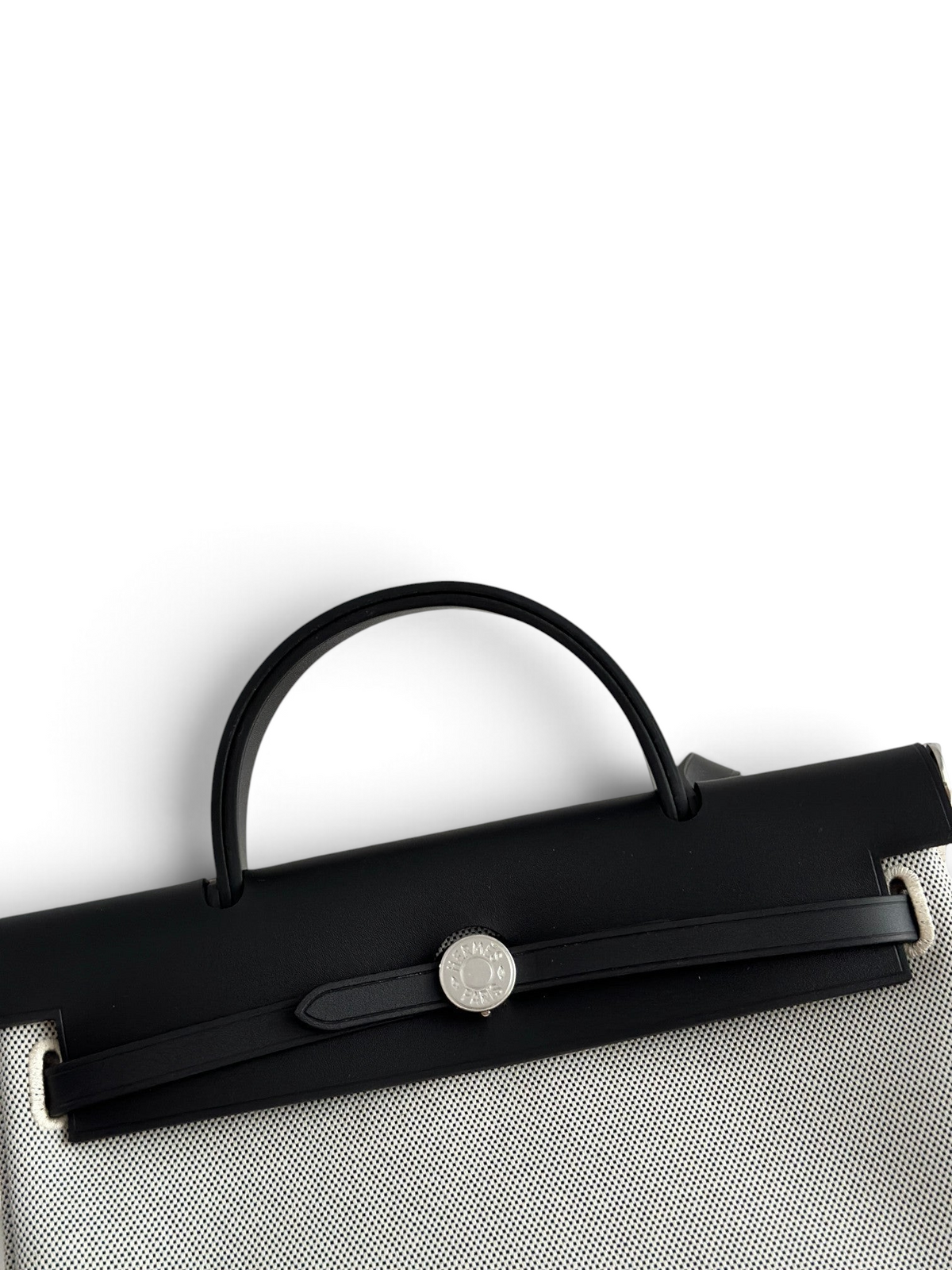 SWORD LUXURY Hermès Herbag 31 çanta, siyah deri kapaklı ve beyaz kanvas gövdeli, ikonik Clou de Selle kilit detaylı.