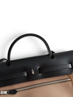 SWORD LUXURY Hermès Herbag 31 siyah deri kapaklı ve kahverengi kanvas gövdeli, ikonik Clou de Selle kilitli çanta.