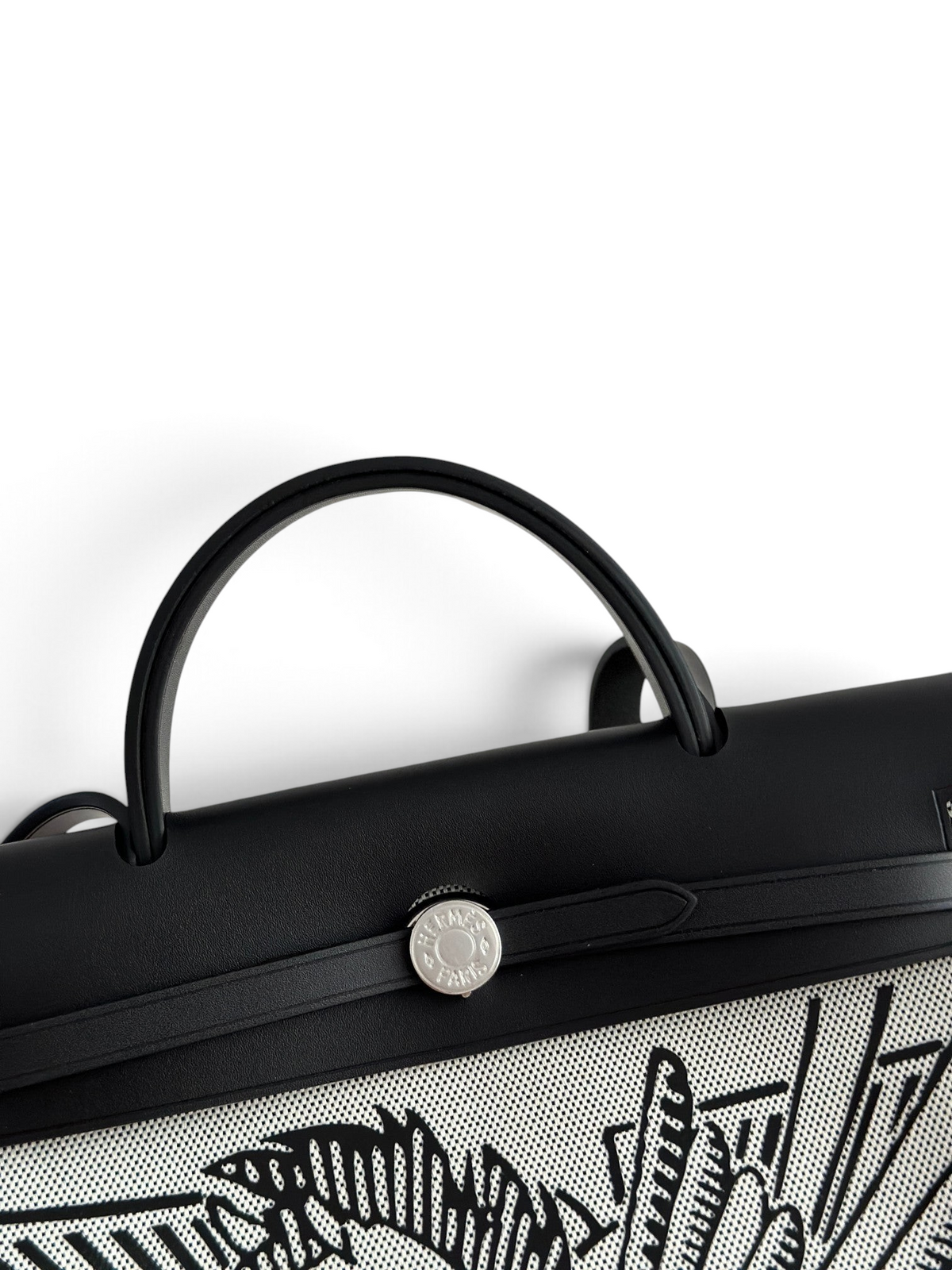 SWORD LUXURY Hermès Herbag 31 çanta, siyah deri kapaklı, Clou de Selle kilitli ve sanatsal baskılı kanvas gövdeli.