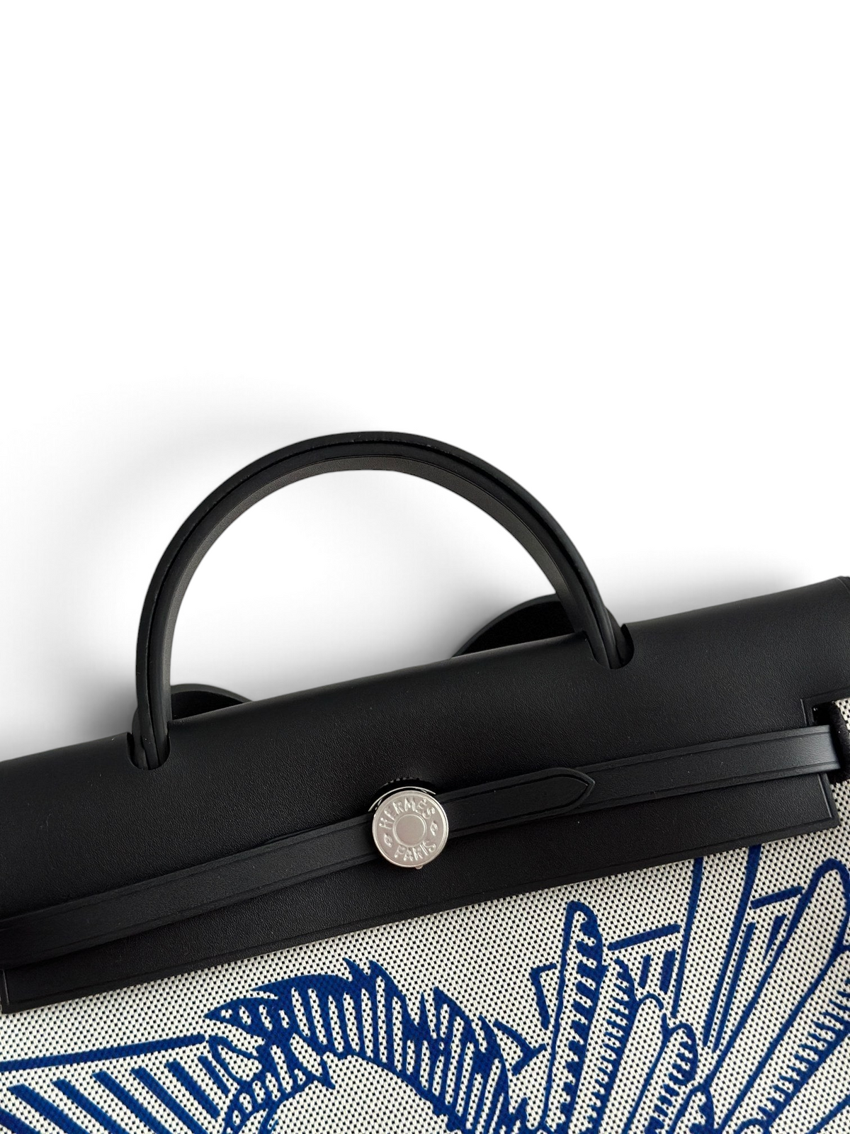 SWORD LUXURY Hermès Herbag 31 çanta, siyah deri kapaklı, mavi desenli kanvas gövdeli ve gümüş Clou de Selle detaylı.