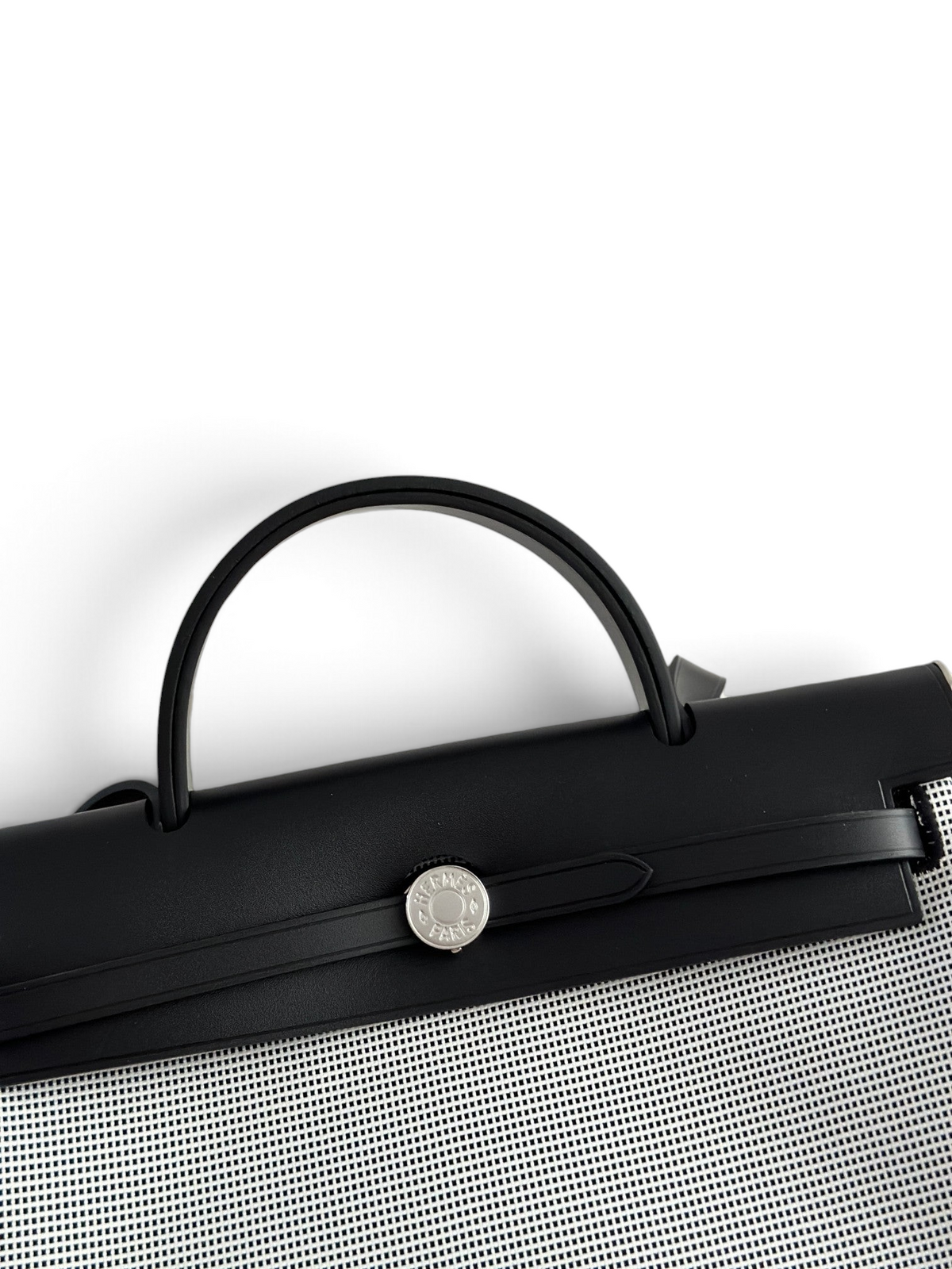 SWORD LUXURY Hermès Herbag 31 çanta, siyah deri kapaklı, gümüş renkli Clou de Selle kilit detaylı ve kanvas gövdeli.