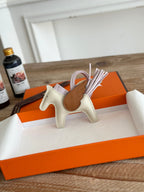 Small horse-shaped keychain in an orange box on a wooden surface with a bottle in the background.