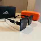 Black sunglasses with brand logo on a reflective surface, with Hermes packaging in the background.
