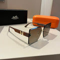 Sunglasses with brown and gold frame on a white surface, with an orange case and black box in the background.