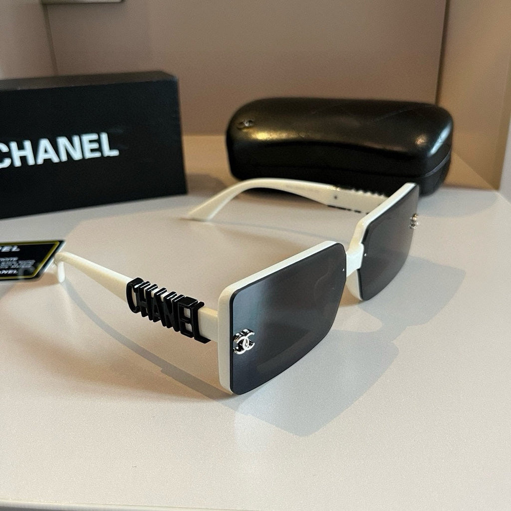 Chanel sunglasses with white frame and black lenses on a reflective surface, with a Chanel box in the background.
