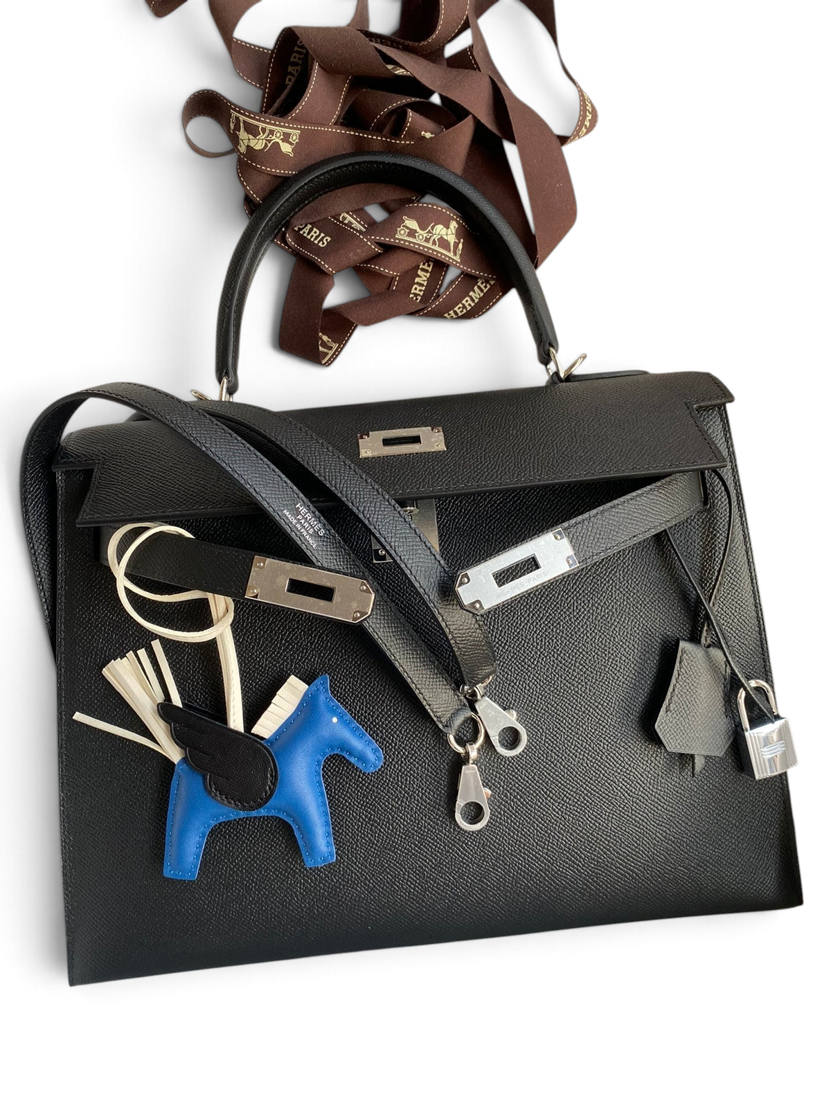 SWORD LUXURY marka siyah Epsom deri Hermès Kelly 32cm çanta, kutusu içinde, omuz askısı ve at figürlü aksesuarı ile.