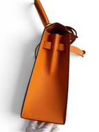 SWORD LUXURY marka turuncu Epsom deri Hermès Kelly 32cm çanta, kutusunda yan profilden detaylı görünüm.