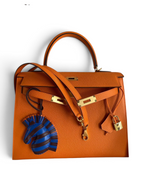 SWORD LUXURY turuncu Epsom deri Hermès Kelly 32cm çanta, altın donanım, kilit, anahtarlar ve zebra çanta süsü ile.