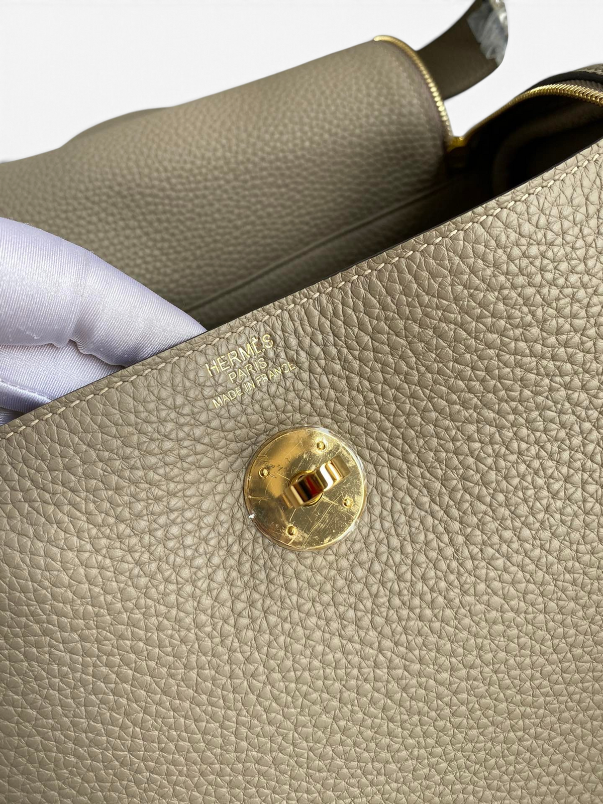 SWORD LUXURY Hermès Lindy 26 çanta, bej renkli dokulu Clemence deri detayları ve altın tonlu döner kilit mekanizması.