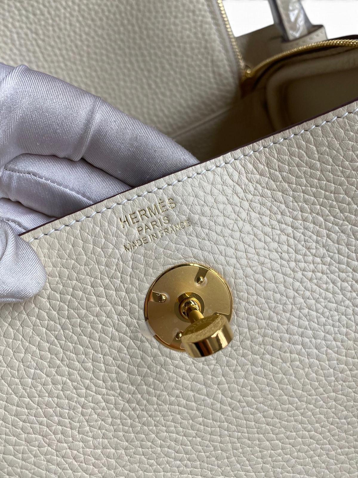 SWORD LUXURY Hermès Lindy 26 çanta, altın rengi kilit detayı ve beyaz Clemence deri dokusu ile yakın çekim.