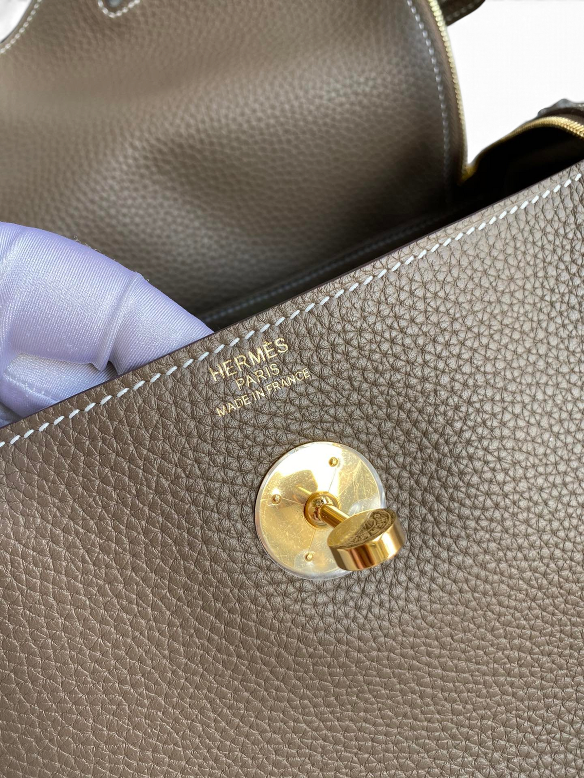 SWORD LUXURY Hermès Lindy 26 çanta, altın rengi kilit detayı ve dokulu Clemence deri yüzeyi ile yakın çekim.