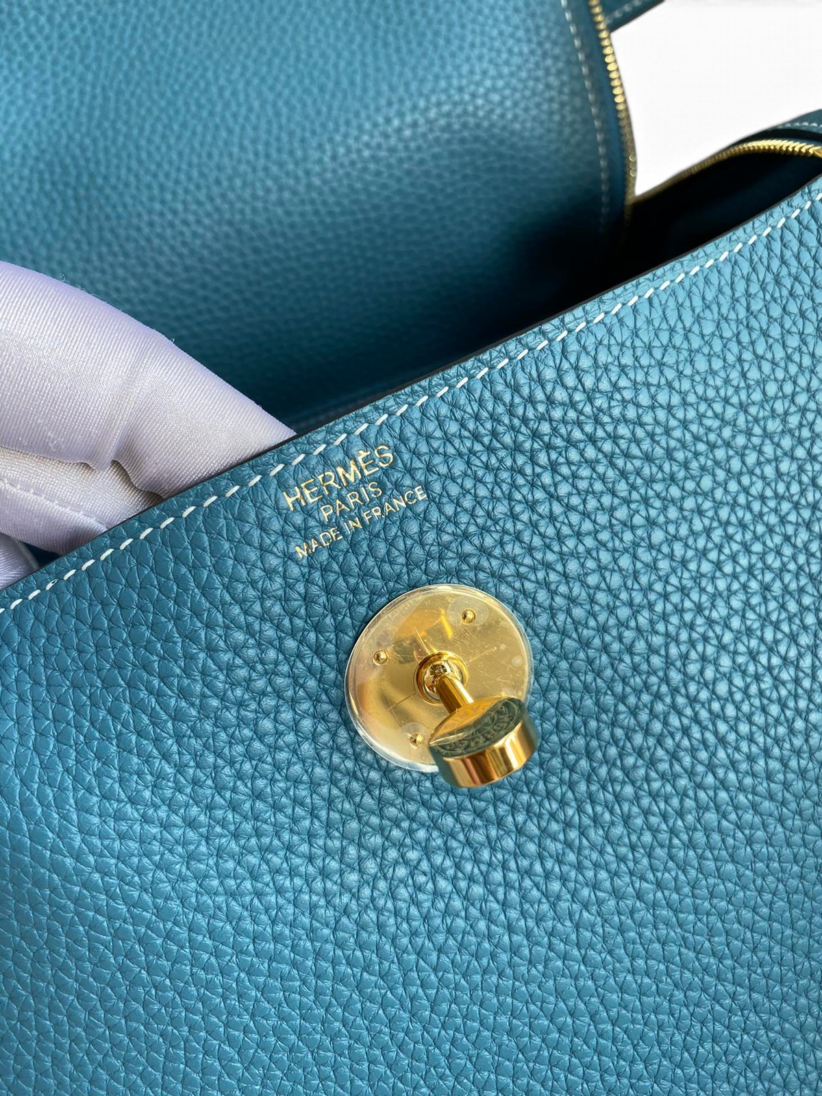 SWORD LUXURY Hermès Lindy 26 çanta, altın rengi kilit detayı ve dokulu mavi Clemence deri yüzeyi ile yakın çekim.