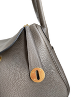 SWORD LUXURY Hermès Lindy 26 çanta, gri Clemence deri dokusu ve altın rengi metal detayları ile yakın çekim.