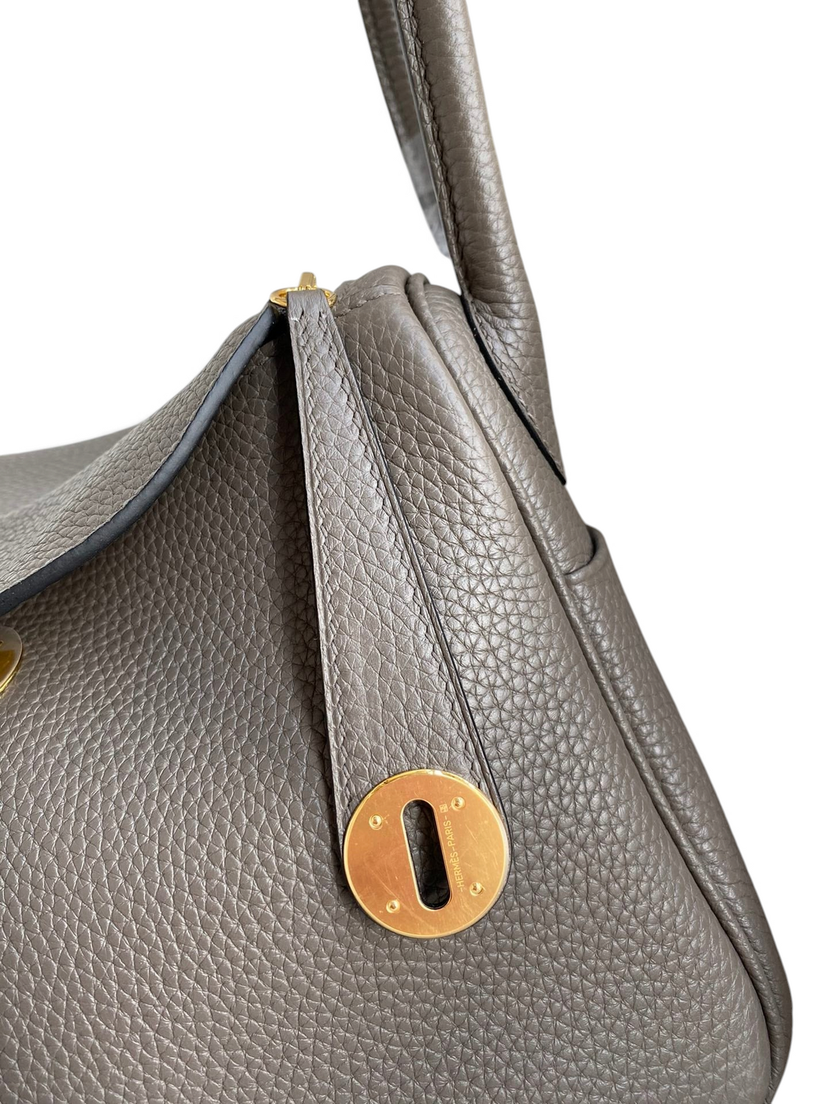 SWORD LUXURY Hermès Lindy 26 çanta, gri Clemence deri dokusu ve altın rengi metal detayları ile yakın çekim.