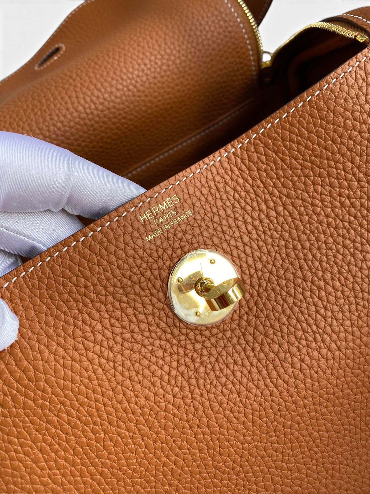 SWORD LUXURY marka taba rengi Clemence deri Hermès Lindy 26 çanta, altın tonlu metal kilit detayı ve logo baskısı.