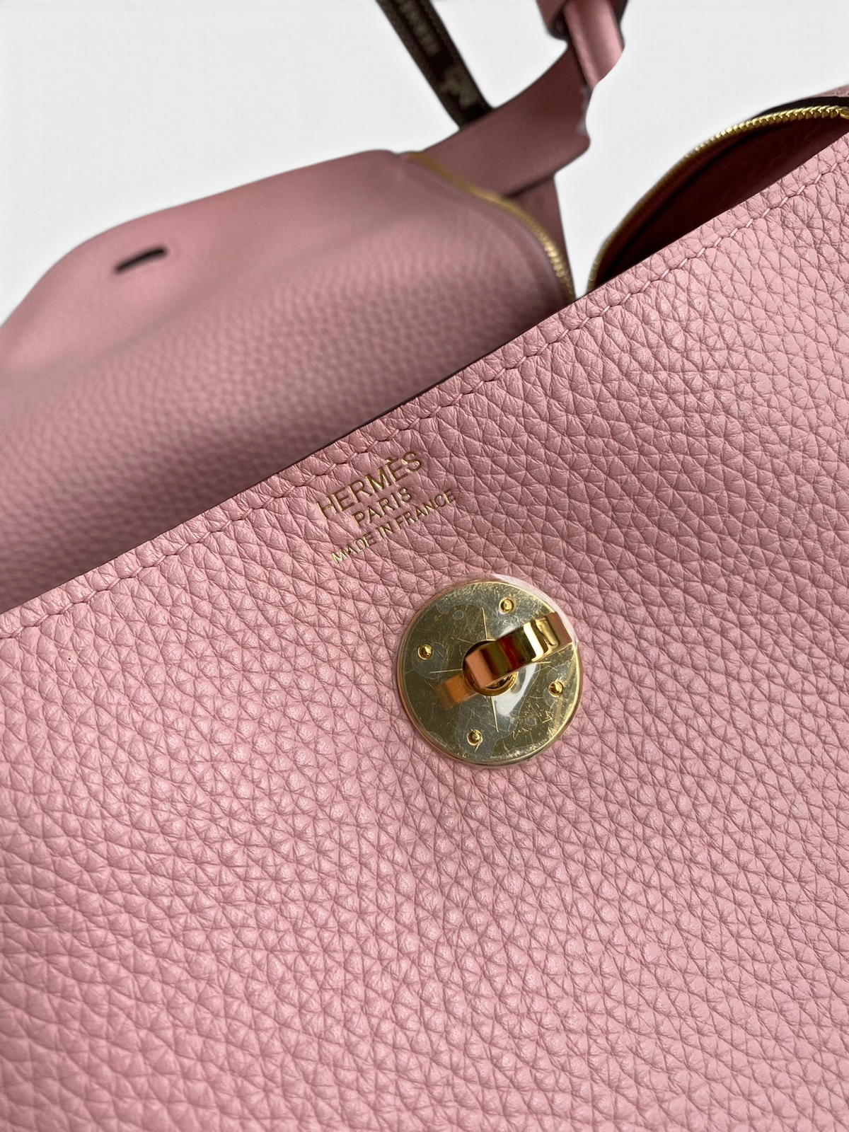 SWORD LUXURY Hermès Lindy 26 çanta, pembe Clemence deri dokusu ve altın rengi metal kilit detayı ile yakından görünüm.