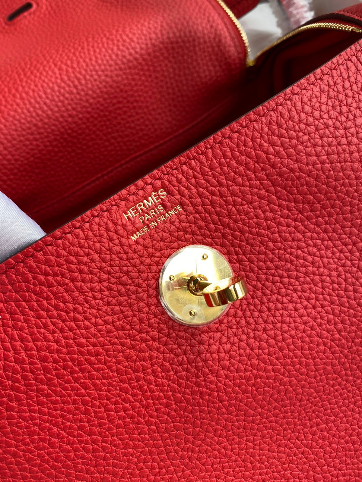 SWORD LUXURY marka kırmızı Clemence deri Hermès Lindy 26 çanta, altın rengi döner kilit detayı ve logo baskısı.