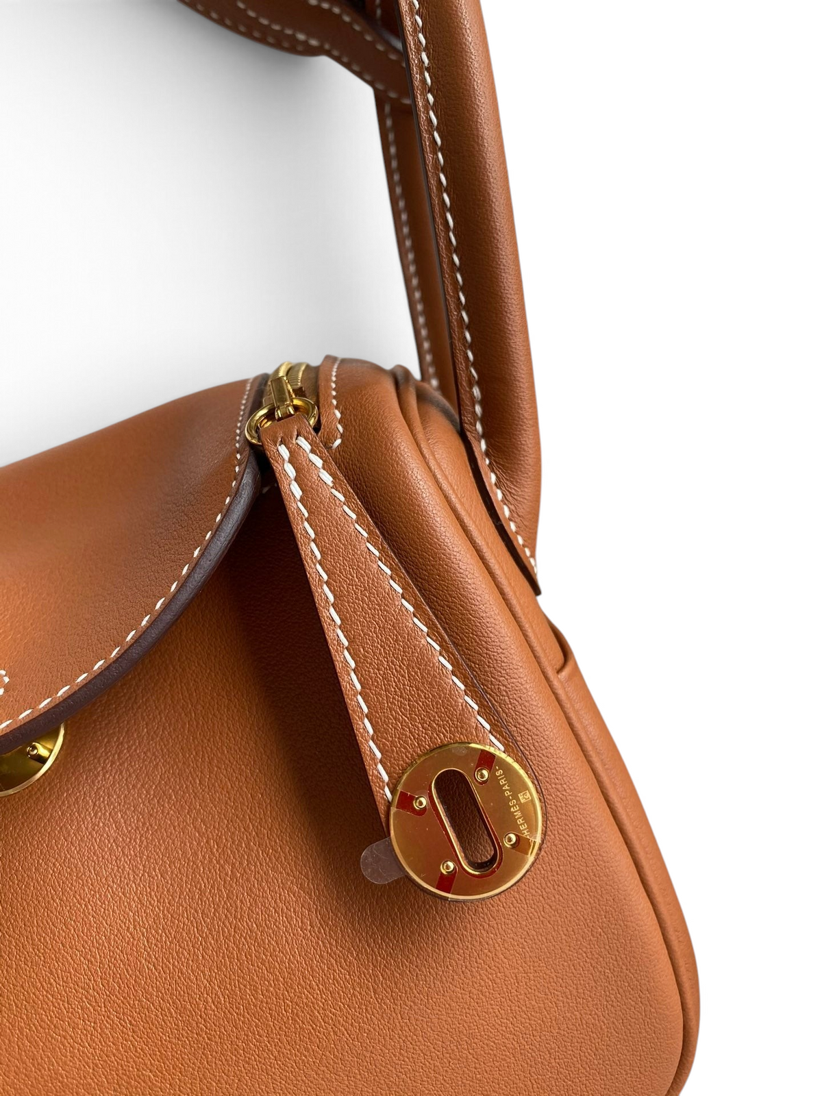 SWORD LUXURY taba rengi Clemence deri Hermès Lindy 19 çanta, altın donanımlı ve ikonik döner kilit detaylı yakın çekim.